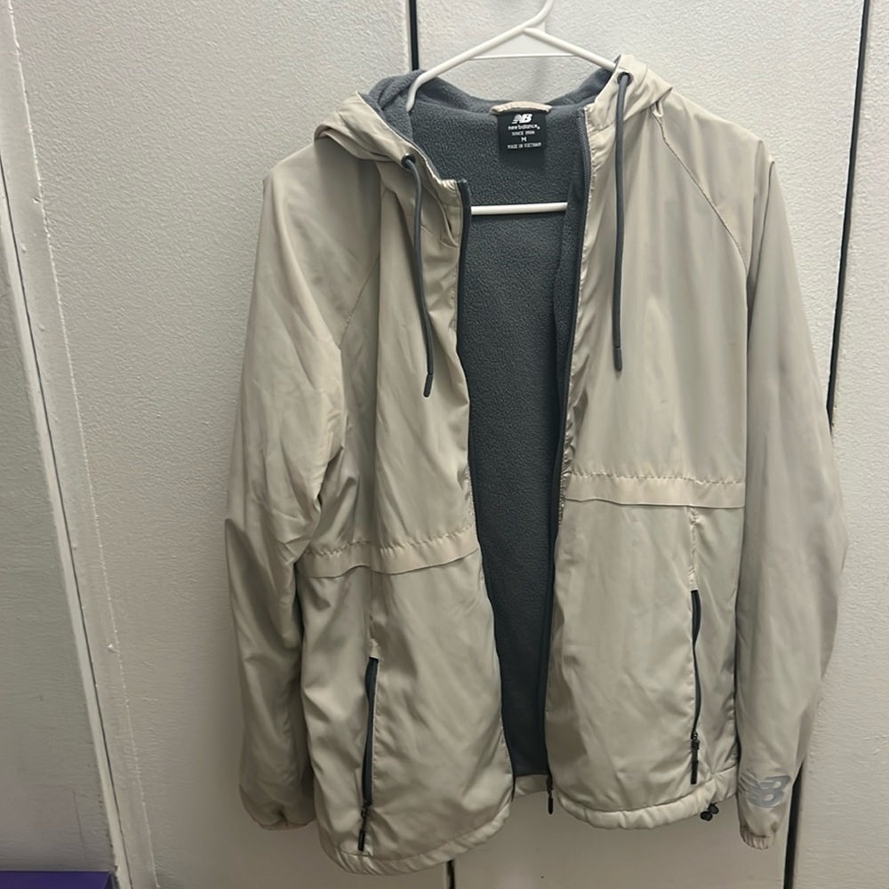 Beige New Balance raincoat w/ fleece lining. Size M. Small pen marking on back.